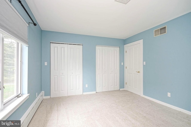 unfurnished bedroom with baseboard heating, two closets, carpet flooring, and baseboards