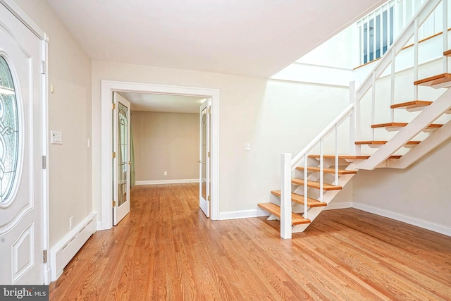 entrance foyer with a baseboard heating unit, light wood-type flooring, stairs, and baseboards