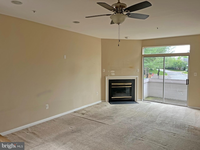 unfurnished living room featuring carpet floors, baseboards, ceiling fan, and a fireplace with flush hearth