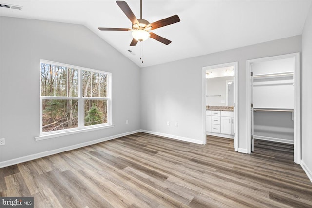 unfurnished bedroom featuring connected bathroom, wood finished floors, a walk in closet, visible vents, and vaulted ceiling