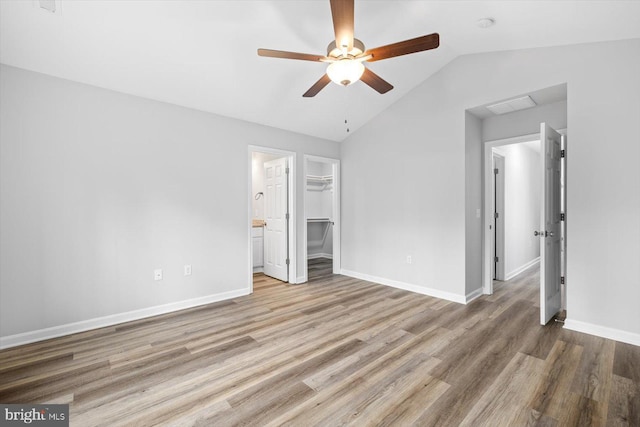 unfurnished bedroom with wood finished floors, visible vents, vaulted ceiling, a walk in closet, and baseboards