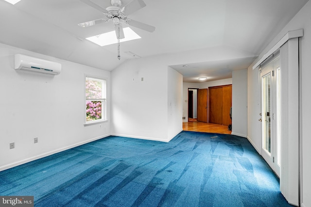 carpeted spare room with vaulted ceiling, a wall mounted AC, ceiling fan, a skylight, and baseboards