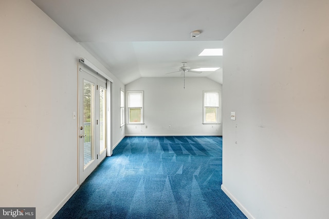 empty room featuring baseboards, carpet floors, vaulted ceiling, a ceiling fan, and a skylight