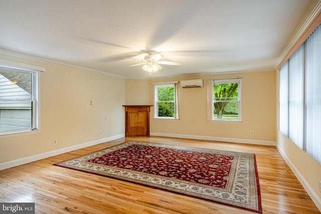 spare room with a wall mounted air conditioner, light wood-style flooring, ceiling fan, crown molding, and baseboards