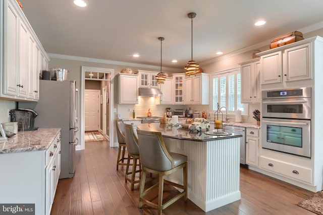 kitchen with under cabinet range hood, crown molding, stainless steel appliances, and a kitchen breakfast bar