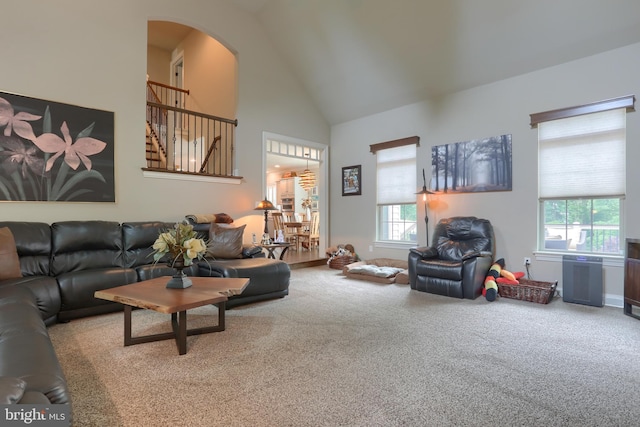 carpeted living room featuring arched walkways and high vaulted ceiling
