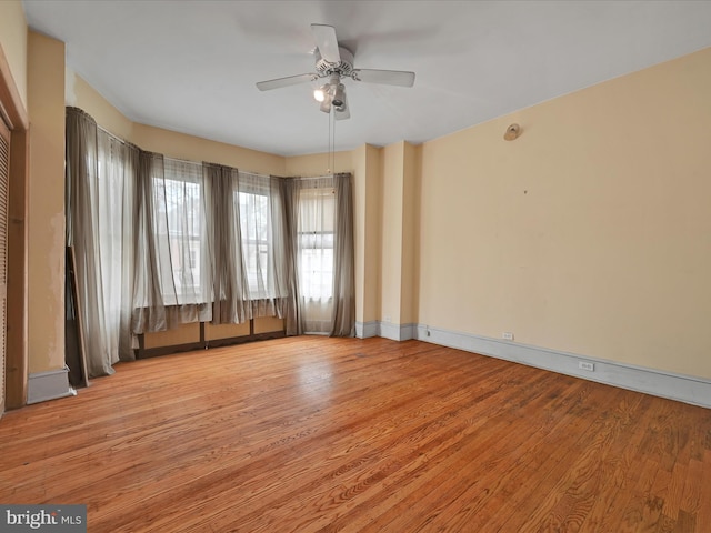 spare room with baseboards, light wood finished floors, and ceiling fan