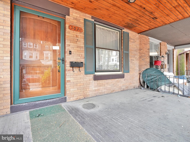 view of exterior entry with brick siding and covered porch