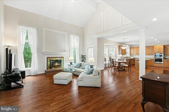 living area featuring high vaulted ceiling, a brick fireplace, dark wood finished floors, and baseboards