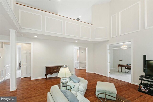 living area featuring a high ceiling, wood finished floors, ornate columns, recessed lighting, and baseboards
