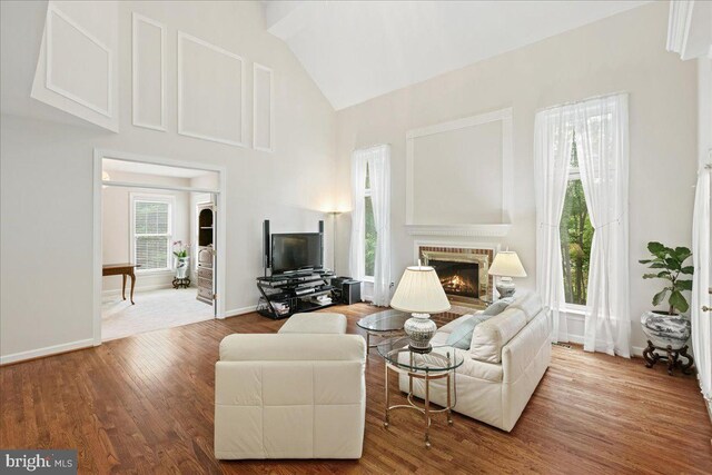 living room featuring a fireplace, wood finished floors, high vaulted ceiling, and baseboards