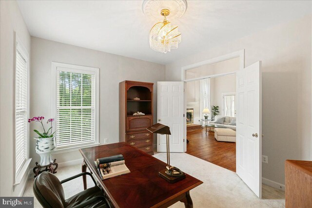 office area featuring a chandelier, carpet floors, baseboards, and a glass covered fireplace