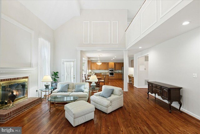 living room featuring high vaulted ceiling, dark wood-style floors, a brick fireplace, baseboards, and recessed lighting