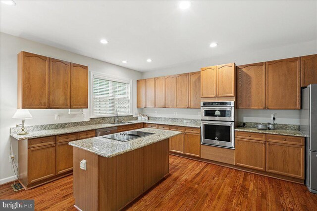 kitchen featuring appliances with stainless steel finishes, a sink, dark wood-style floors, light stone countertops, and a kitchen island