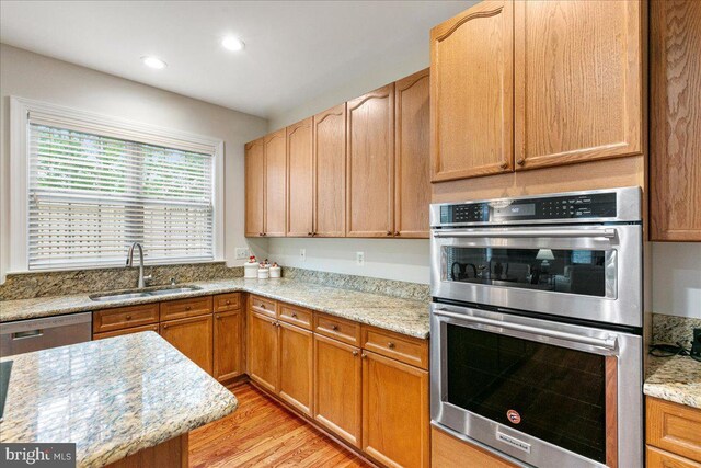 kitchen featuring appliances with stainless steel finishes, a sink, light wood-style flooring, light stone counters, and recessed lighting