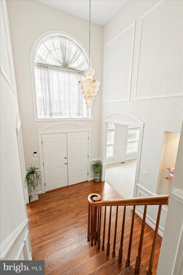 foyer entrance with a chandelier, wood finished floors, a high ceiling, and stairs