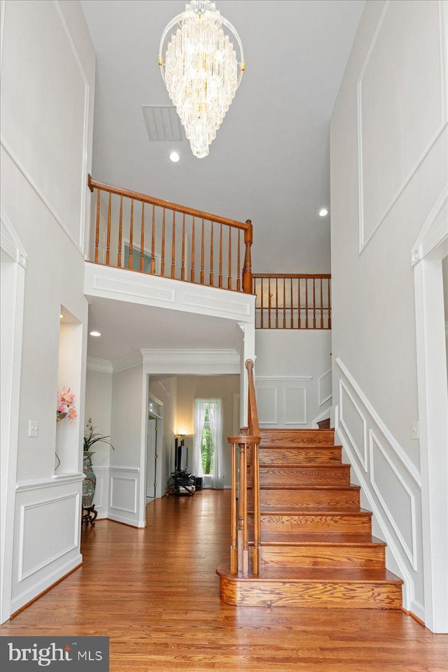 staircase with a decorative wall, wood finished floors, a chandelier, a high ceiling, and ornamental molding