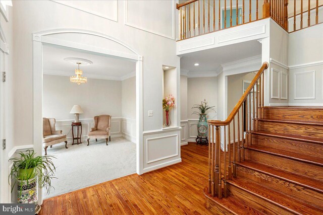 entrance foyer with crown molding, a decorative wall, stairs, wood finished floors, and a chandelier