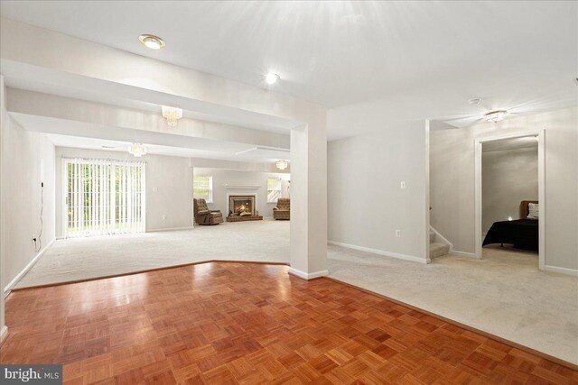 unfurnished living room featuring baseboards, stairway, a warm lit fireplace, and carpet flooring