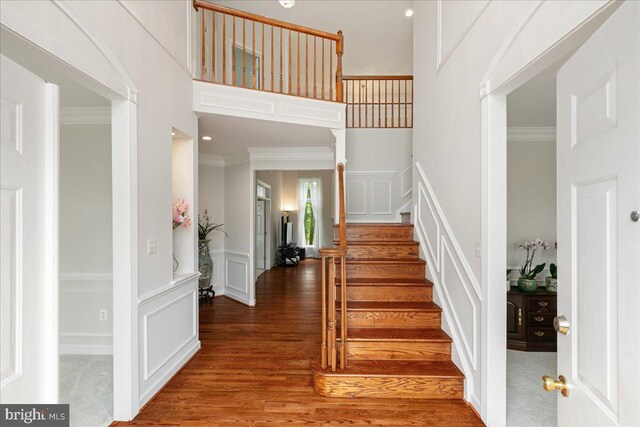 foyer entrance with a decorative wall, wood finished floors, stairway, crown molding, and a high ceiling