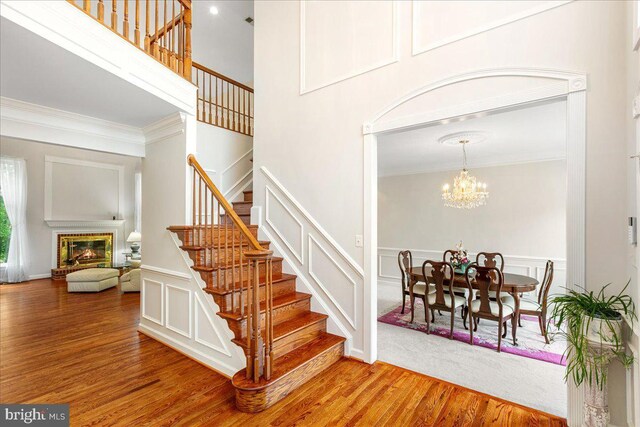 stairway featuring a decorative wall, ornamental molding, wood finished floors, a glass covered fireplace, and a chandelier