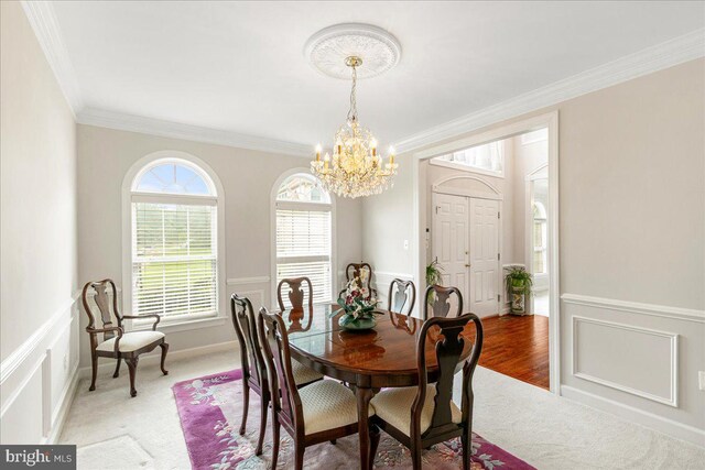 dining space with a chandelier, ornamental molding, wainscoting, light colored carpet, and a decorative wall
