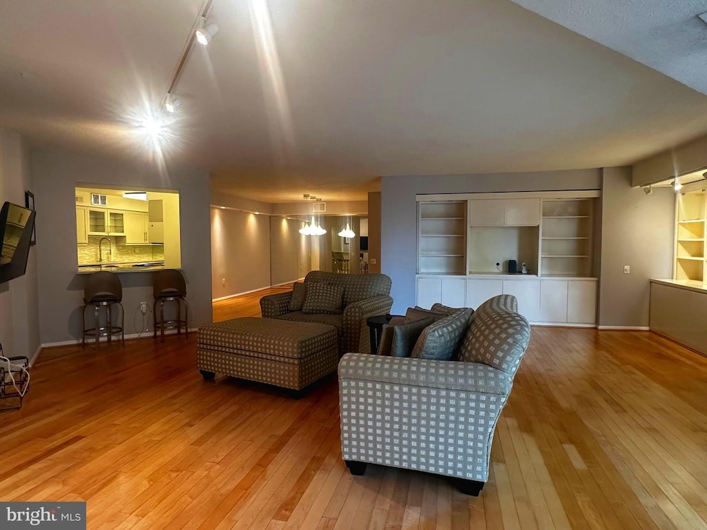 living area featuring baseboards, wood-type flooring, built in features, and track lighting