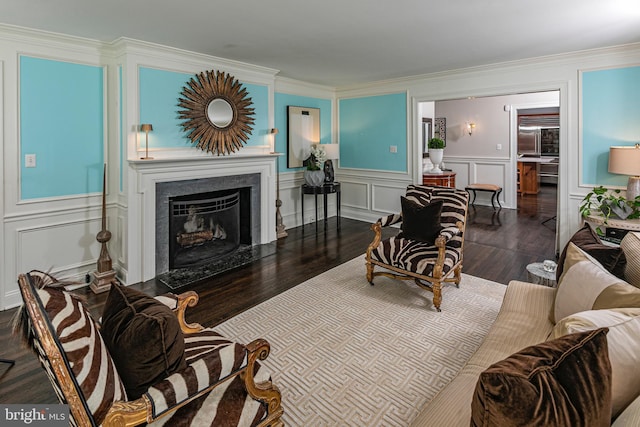 living room with ornamental molding, a decorative wall, a fireplace with flush hearth, and wood finished floors
