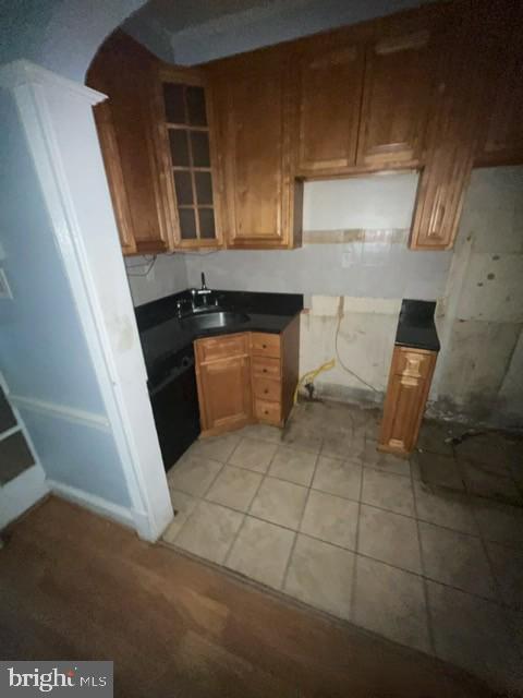 kitchen with light tile patterned flooring, a sink, arched walkways, brown cabinets, and dark countertops