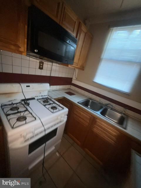 kitchen featuring a sink, brown cabinets, white gas range, black microwave, and backsplash