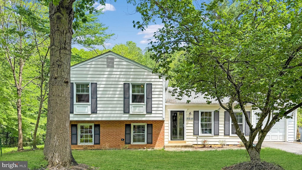 tri-level home featuring a front yard, brick siding, a garage, and driveway