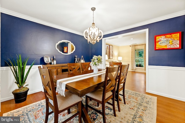 dining space featuring a chandelier, crown molding, wood finished floors, and a wainscoted wall