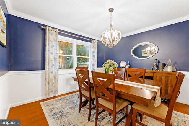 dining space featuring a chandelier, ornamental molding, wood finished floors, and a wainscoted wall