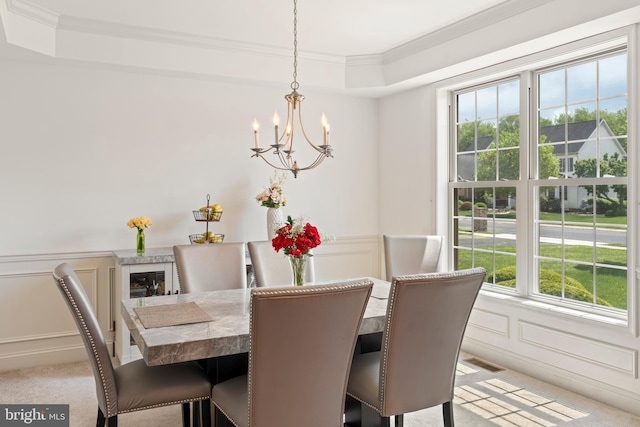 dining space with a chandelier, light carpet, crown molding, and a decorative wall