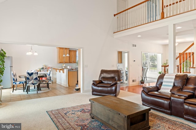 living room featuring a towering ceiling, visible vents, stairway, a chandelier, and light carpet