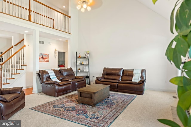 carpeted living room featuring a ceiling fan, baseboards, visible vents, stairs, and high vaulted ceiling