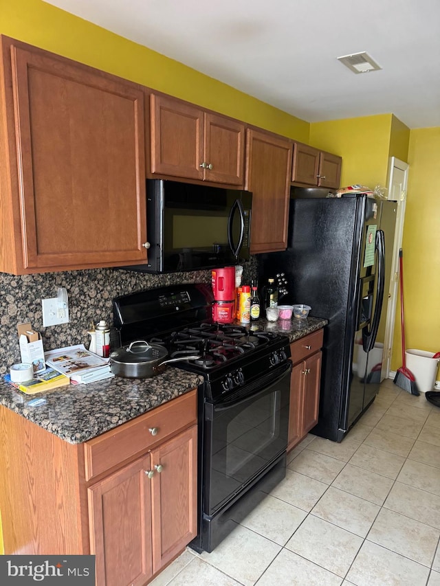 kitchen featuring backsplash, black appliances, light tile patterned floors, and dark stone countertops