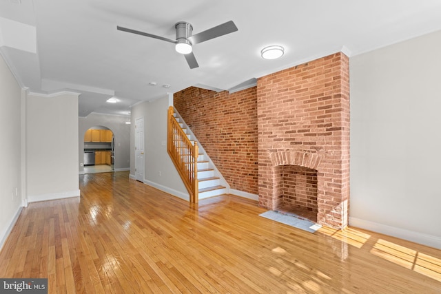 722 S Clinton St, Baltimore, MD 21224 - unfurnished living room featuring arched walkways, hardwood / wood-style flooring, a ceiling fan, stairs, and a fireplace