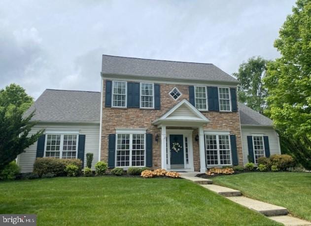 colonial home featuring stone siding and a front yard