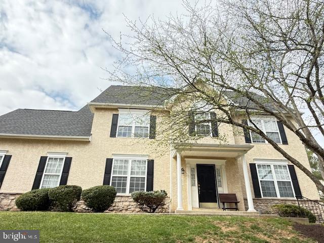 colonial home with stucco siding, stone siding, and a front yard
