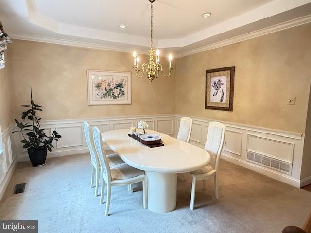 dining area with a tray ceiling, an inviting chandelier, visible vents, and light carpet