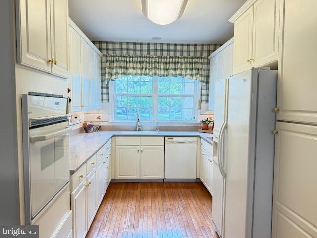 kitchen featuring light countertops, white cabinetry, a sink, and white appliances