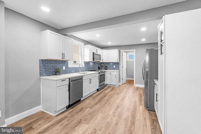 kitchen featuring baseboards, a sink, backsplash, light wood-style floors, and appliances with stainless steel finishes