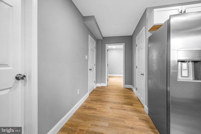 corridor with light wood-type flooring and baseboards