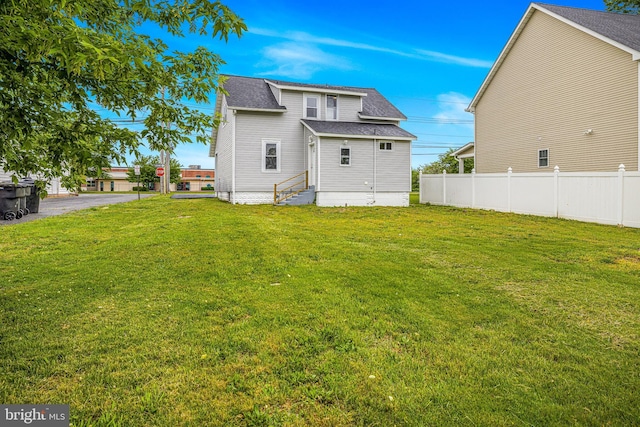 rear view of property with a lawn, entry steps, roof with shingles, and fence