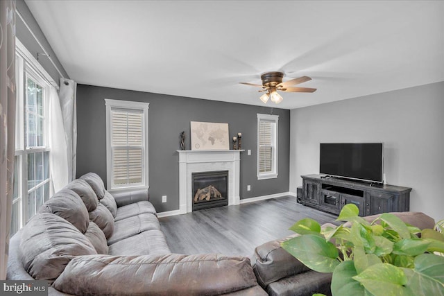living area featuring baseboards, a glass covered fireplace, ceiling fan, and wood finished floors