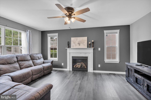living area with a ceiling fan, baseboards, a glass covered fireplace, and wood finished floors