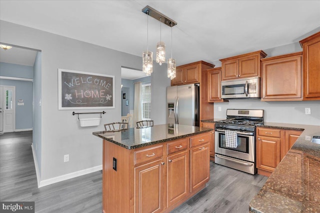 kitchen with stainless steel appliances, a center island, dark stone countertops, and wood finished floors