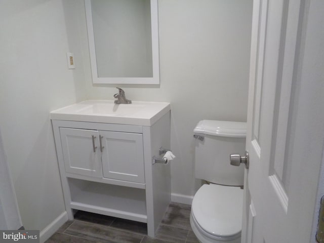 half bath featuring vanity, toilet, baseboards, and wood finished floors
