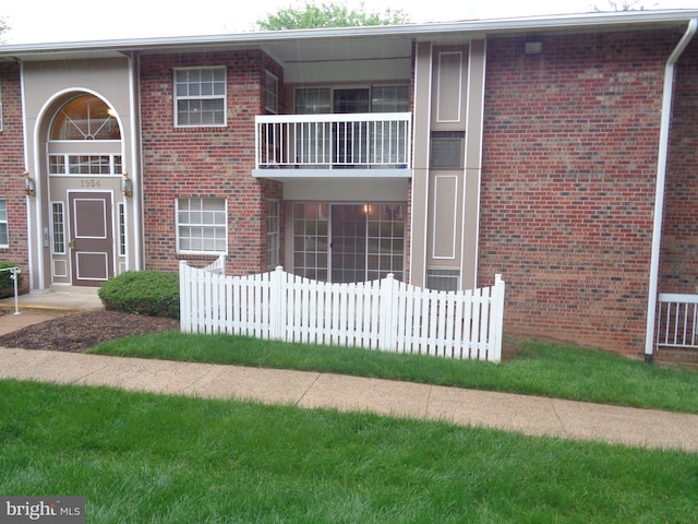 view of front facade with fence, brick siding, and a balcony